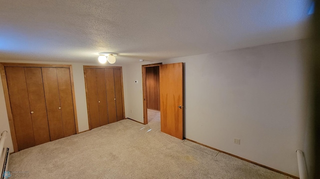 unfurnished bedroom with two closets, light colored carpet, and a textured ceiling