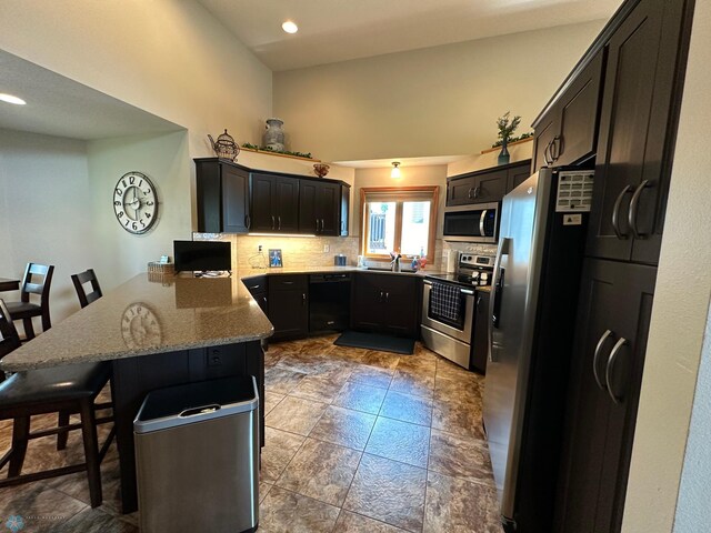 kitchen featuring backsplash, light stone countertops, stainless steel appliances, kitchen peninsula, and a breakfast bar