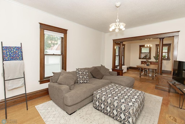 living room featuring light hardwood / wood-style flooring, a chandelier, ornate columns, a textured ceiling, and crown molding