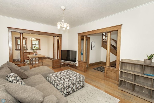 living room with light hardwood / wood-style floors, an inviting chandelier, crown molding, decorative columns, and a textured ceiling