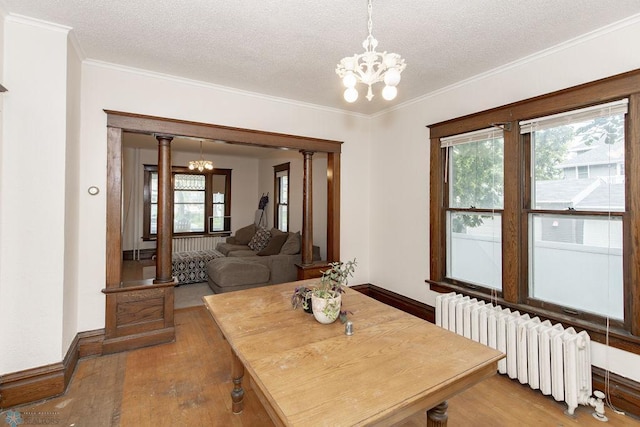 dining space featuring radiator heating unit, hardwood / wood-style floors, a textured ceiling, and a chandelier