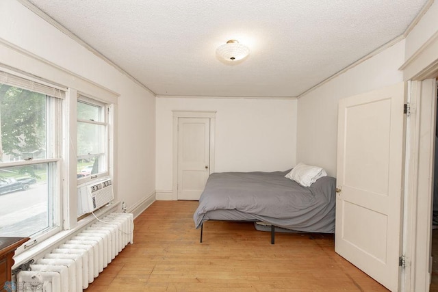 bedroom with light wood-type flooring, a textured ceiling, ornamental molding, and radiator