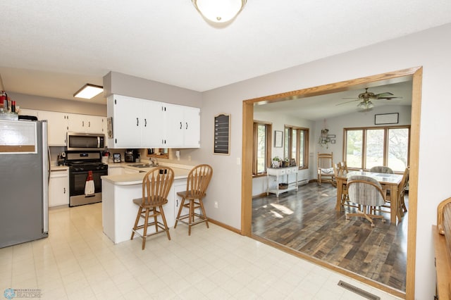 kitchen featuring a breakfast bar, vaulted ceiling, light hardwood / wood-style floors, appliances with stainless steel finishes, and kitchen peninsula