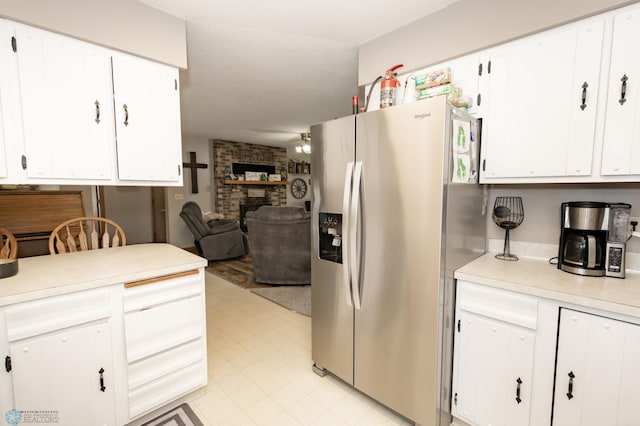 kitchen featuring a fireplace, stainless steel refrigerator with ice dispenser, light tile patterned floors, brick wall, and white cabinets