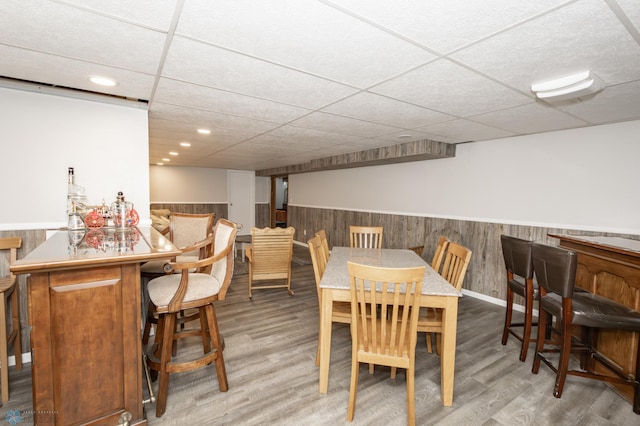 dining area featuring light hardwood / wood-style floors, a drop ceiling, and bar