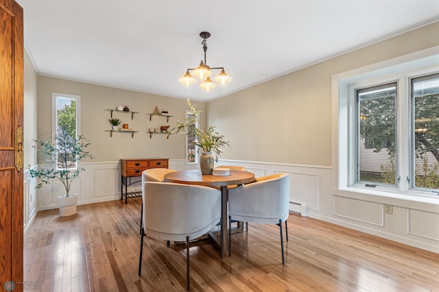 dining room with an inviting chandelier, baseboard heating, light wood-type flooring, and crown molding