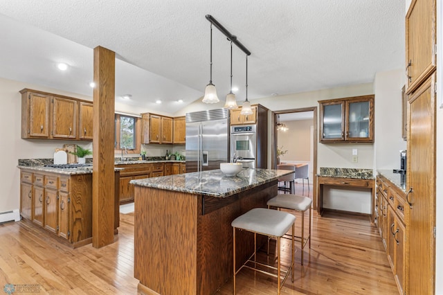 kitchen featuring appliances with stainless steel finishes, light wood-type flooring, a kitchen island, dark stone counters, and vaulted ceiling