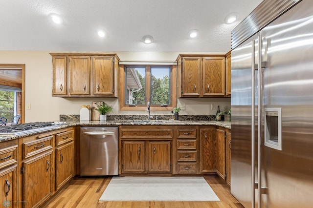 kitchen featuring a textured ceiling, stainless steel appliances, light wood-type flooring, and dark stone countertops