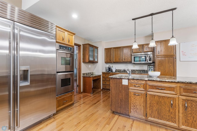 kitchen featuring dark stone counters, decorative light fixtures, light wood-type flooring, appliances with stainless steel finishes, and a textured ceiling