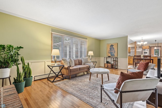 living room featuring a baseboard heating unit, a textured ceiling, ornamental molding, light hardwood / wood-style floors, and a notable chandelier