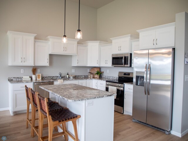 kitchen with a kitchen island, stainless steel appliances, a high ceiling, light hardwood / wood-style flooring, and decorative light fixtures