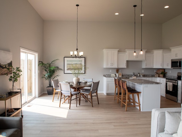 kitchen with appliances with stainless steel finishes, a towering ceiling, light stone counters, and decorative light fixtures