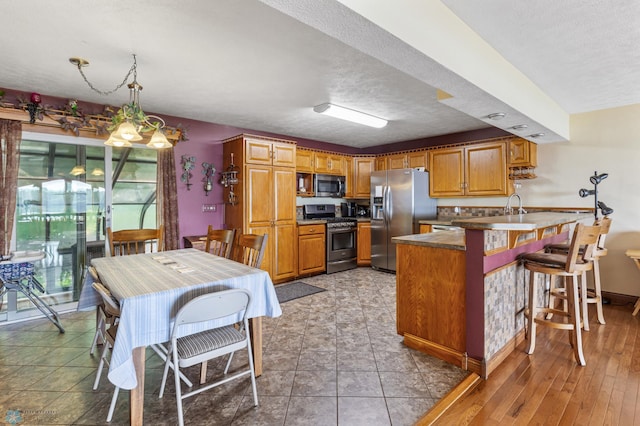 kitchen featuring appliances with stainless steel finishes, decorative light fixtures, light hardwood / wood-style floors, a textured ceiling, and a kitchen breakfast bar