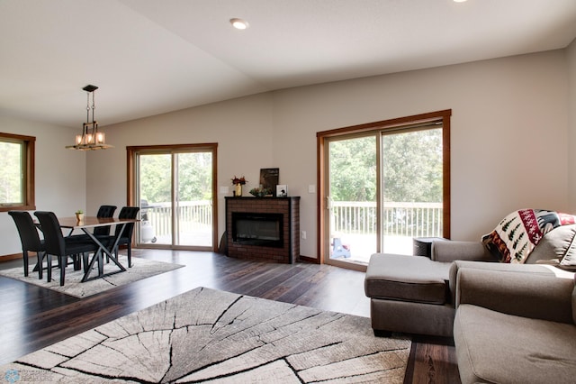 living room with dark hardwood / wood-style floors, vaulted ceiling, a notable chandelier, and a brick fireplace