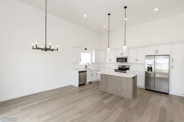 kitchen featuring white cabinets, light hardwood / wood-style flooring, stainless steel appliances, a high ceiling, and a kitchen island