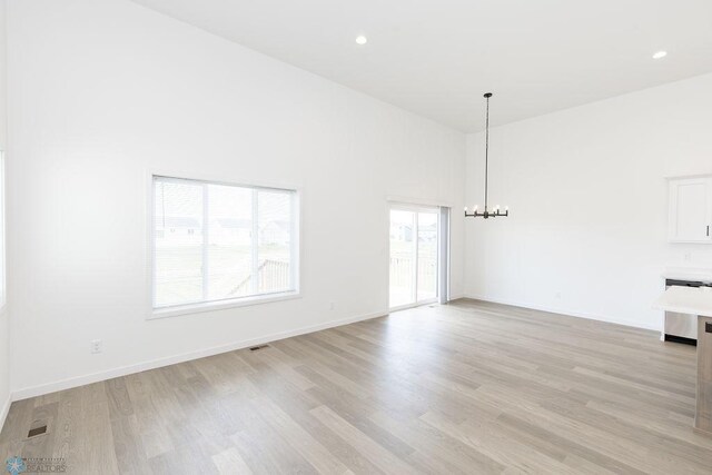 empty room featuring light wood-type flooring, a towering ceiling, and a notable chandelier