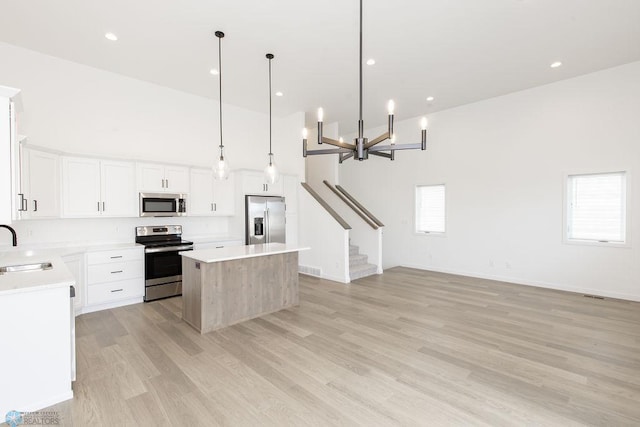 kitchen with white cabinetry, stainless steel appliances, a center island, a towering ceiling, and light hardwood / wood-style floors