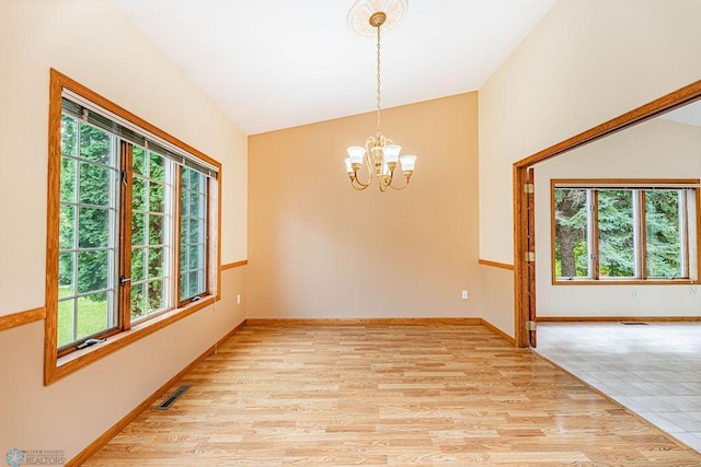 spare room featuring light wood-type flooring, lofted ceiling, a healthy amount of sunlight, and an inviting chandelier