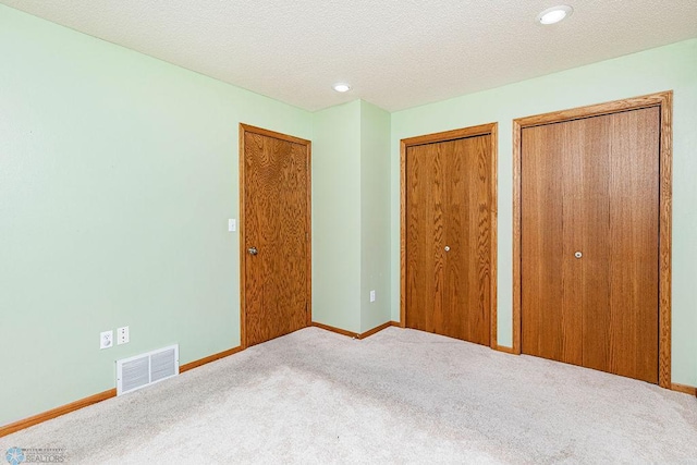 unfurnished bedroom with multiple closets, a textured ceiling, and carpet