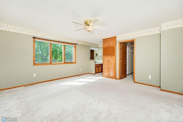 unfurnished bedroom featuring light carpet, connected bathroom, ceiling fan, a closet, and a spacious closet