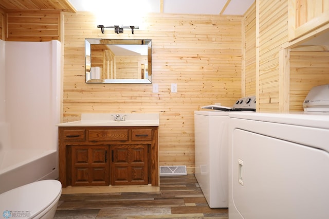 washroom featuring dark hardwood / wood-style flooring, wooden walls, and washing machine and clothes dryer