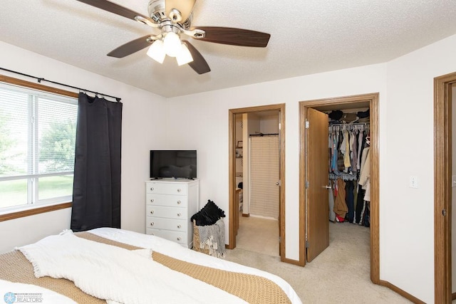 bedroom with a walk in closet, a closet, connected bathroom, light colored carpet, and ceiling fan