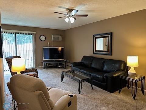 living room featuring a wall mounted AC, carpet flooring, a textured ceiling, and ceiling fan