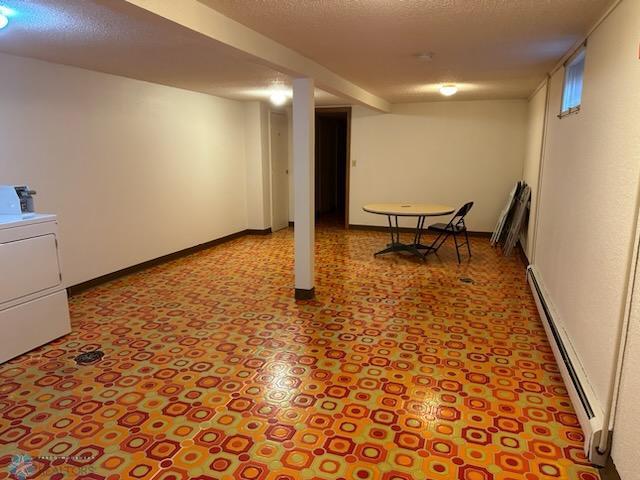 basement with a textured ceiling, a baseboard radiator, and washer / clothes dryer