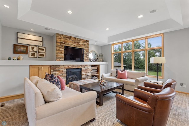 living room featuring light carpet, a stone fireplace, and a tray ceiling