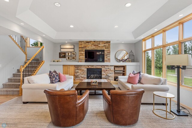 living room with a stone fireplace, light wood-type flooring, and a raised ceiling