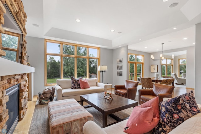 living room with a stone fireplace, light hardwood / wood-style flooring, a chandelier, and a raised ceiling