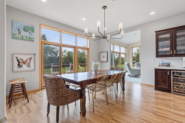 dining area featuring light hardwood / wood-style floors, an inviting chandelier, beverage cooler, and vaulted ceiling