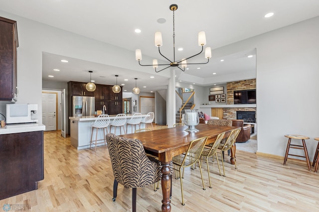 dining area featuring sink, a notable chandelier, a stone fireplace, and light hardwood / wood-style flooring