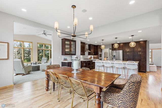 dining room with vaulted ceiling, ceiling fan with notable chandelier, and light hardwood / wood-style floors