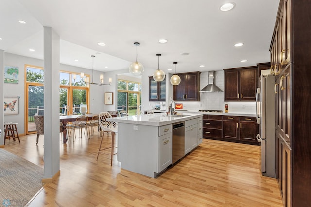 kitchen featuring pendant lighting, wall chimney range hood, light hardwood / wood-style flooring, and an island with sink