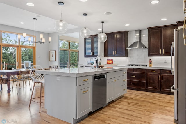 kitchen featuring sink, hanging light fixtures, light hardwood / wood-style floors, stainless steel appliances, and a center island with sink