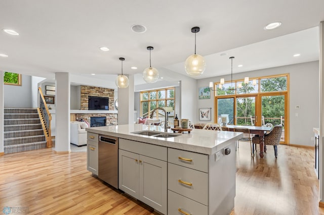 kitchen featuring stainless steel dishwasher, light hardwood / wood-style flooring, a kitchen island with sink, and sink