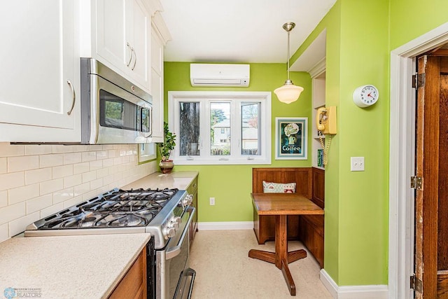 kitchen with a wall mounted air conditioner, backsplash, hanging light fixtures, appliances with stainless steel finishes, and white cabinets