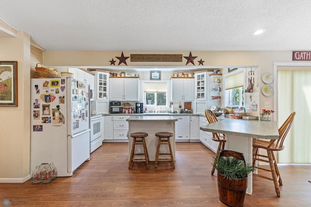 kitchen featuring white appliances, a kitchen bar, a kitchen island, and white cabinetry