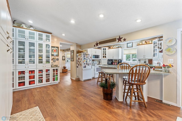 kitchen featuring vaulted ceiling, white appliances, hardwood / wood-style floors, kitchen peninsula, and white cabinets