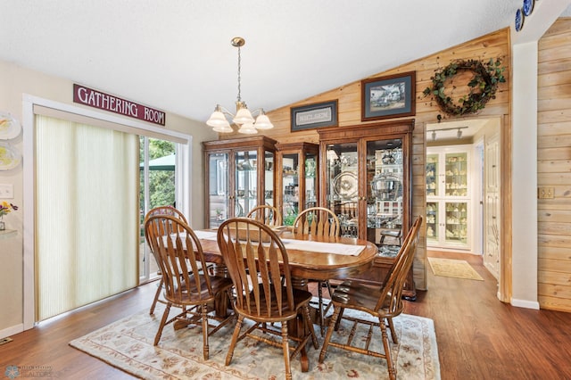 dining area featuring vaulted ceiling, hardwood / wood-style flooring, an inviting chandelier, and wooden walls