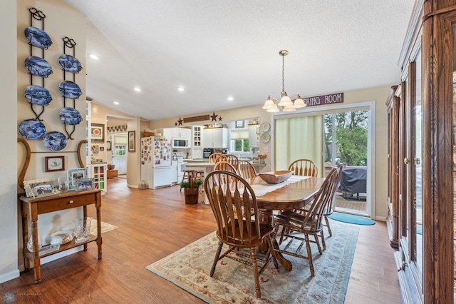 dining area with lofted ceiling, light wood-type flooring, an inviting chandelier, and a textured ceiling