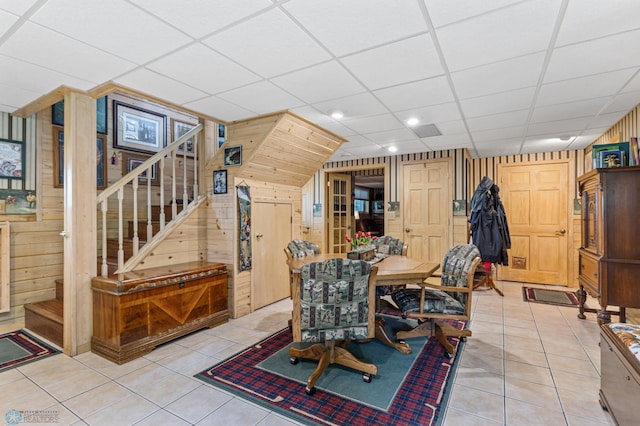 interior space with a paneled ceiling, light tile patterned floors, and wooden walls