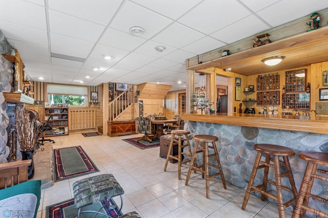 bar featuring light tile patterned floors, refrigerator, and a drop ceiling