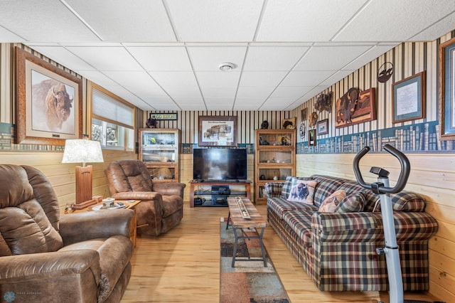 living room with a paneled ceiling, wood walls, and light hardwood / wood-style floors