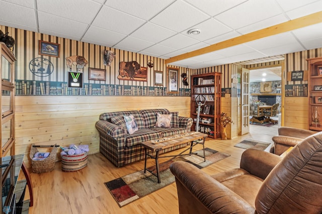 living room with light wood-type flooring, wood walls, and a paneled ceiling