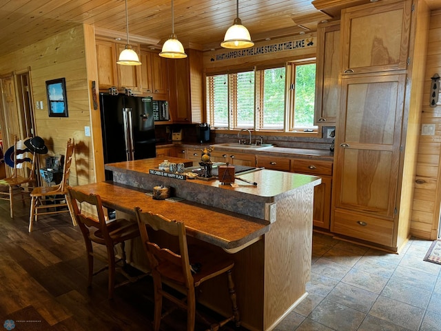 kitchen featuring hanging light fixtures, wood walls, a kitchen island, black appliances, and wooden ceiling