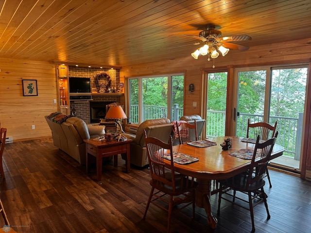 dining space featuring wood walls, a brick fireplace, dark hardwood / wood-style flooring, and ceiling fan