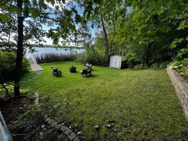 view of yard featuring a water view, a fire pit, and a storage unit