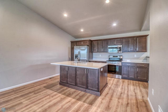 kitchen featuring a kitchen island with sink, light wood-type flooring, stainless steel appliances, vaulted ceiling, and dark brown cabinetry